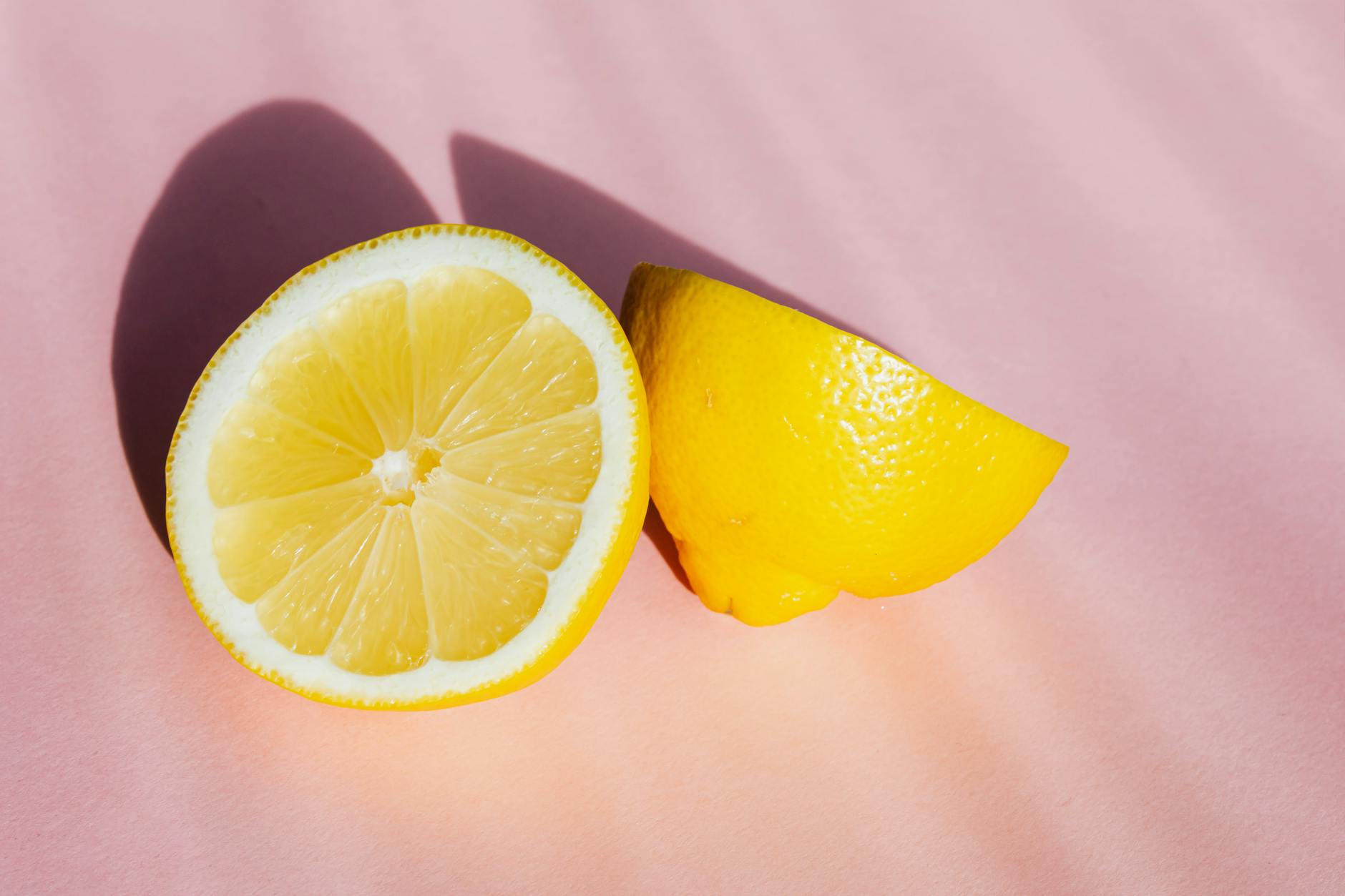 Fresh lemon halves on pink background in bright sunlight