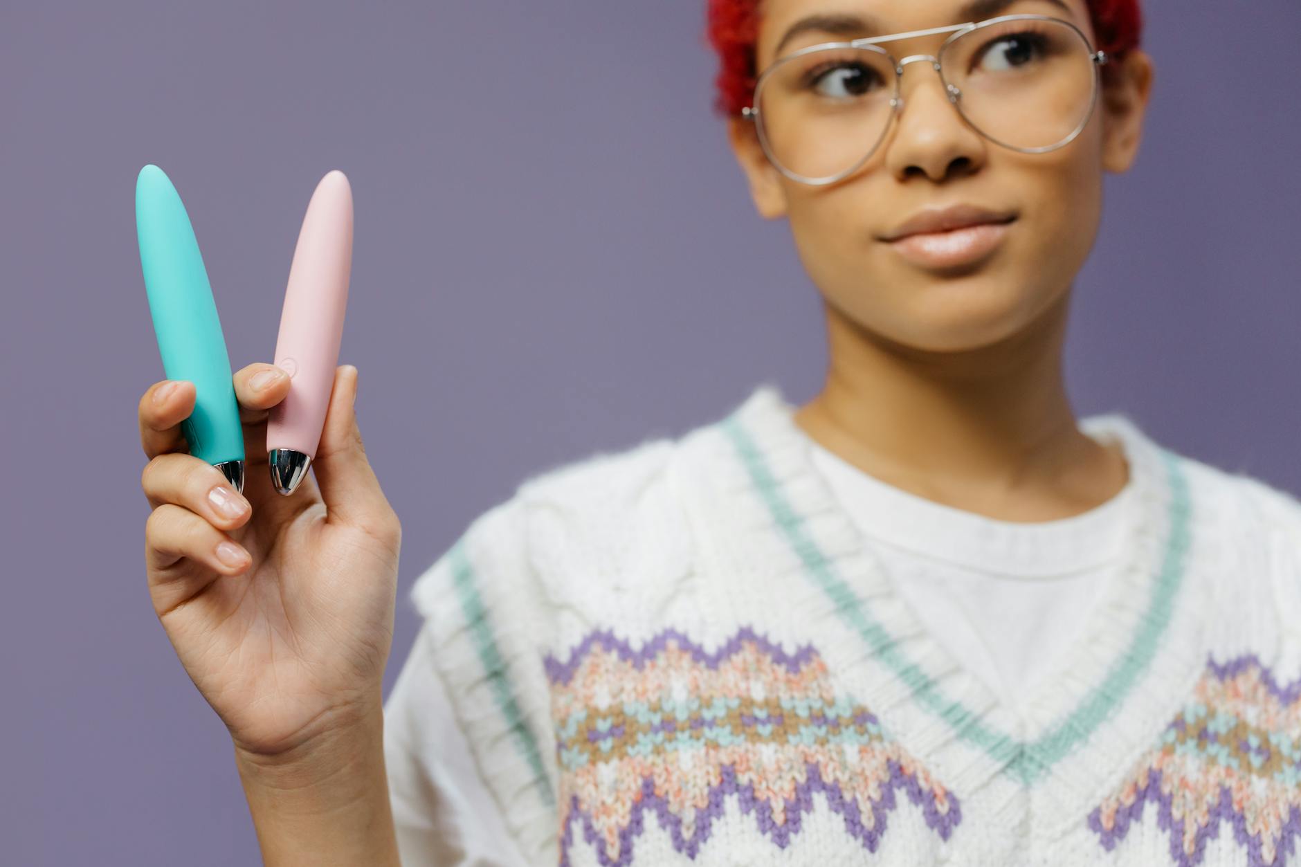 A woman holding a colorful vibrator against a purple background, ready to explore pleasure