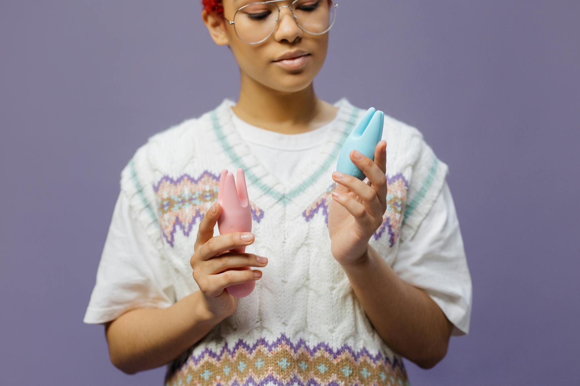 Close-up of hands holding a sleek blue vibrator against a purple background