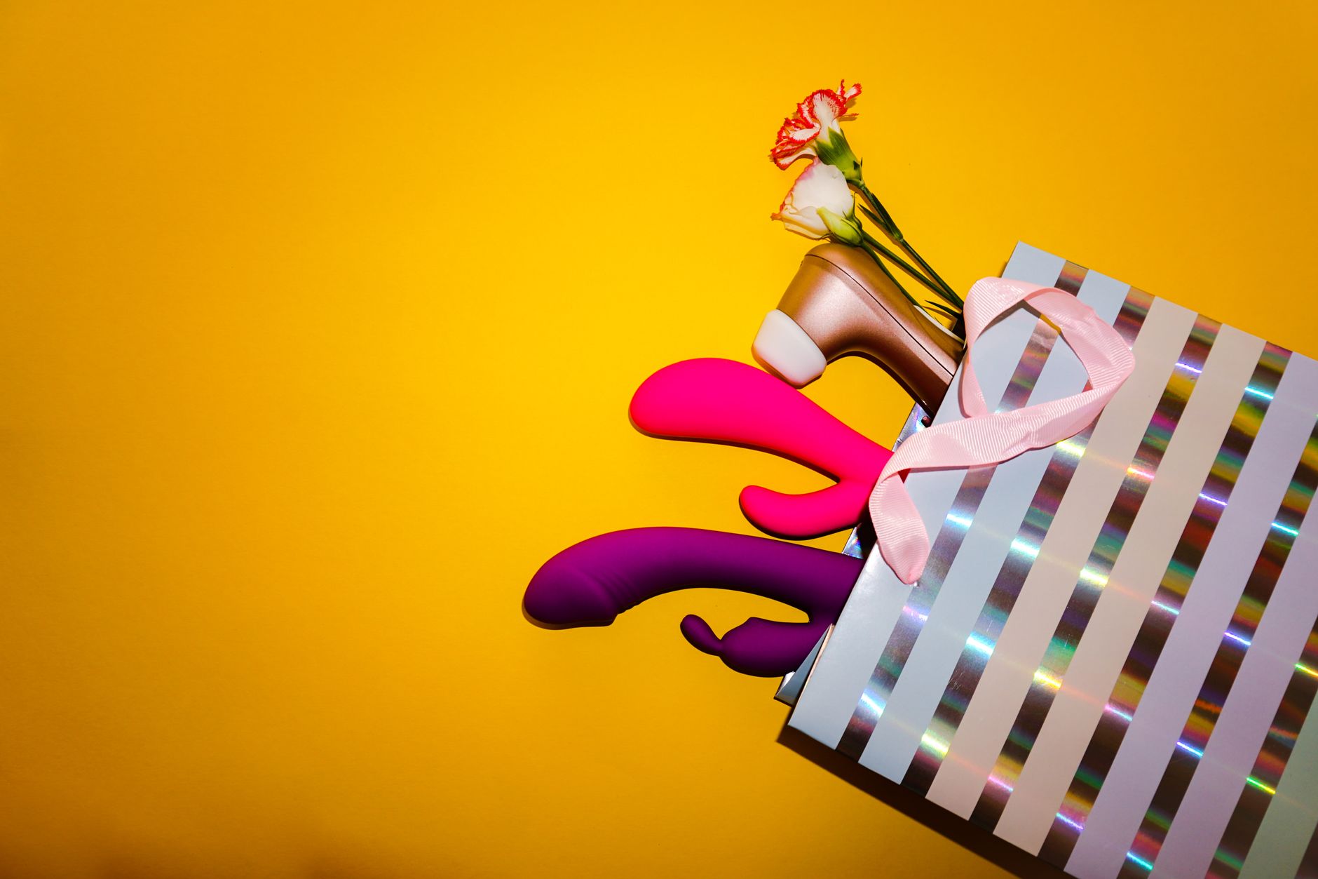 Vibrateurs colorés avec des fleurs dans un sac cadeau holographique sur fond jaune