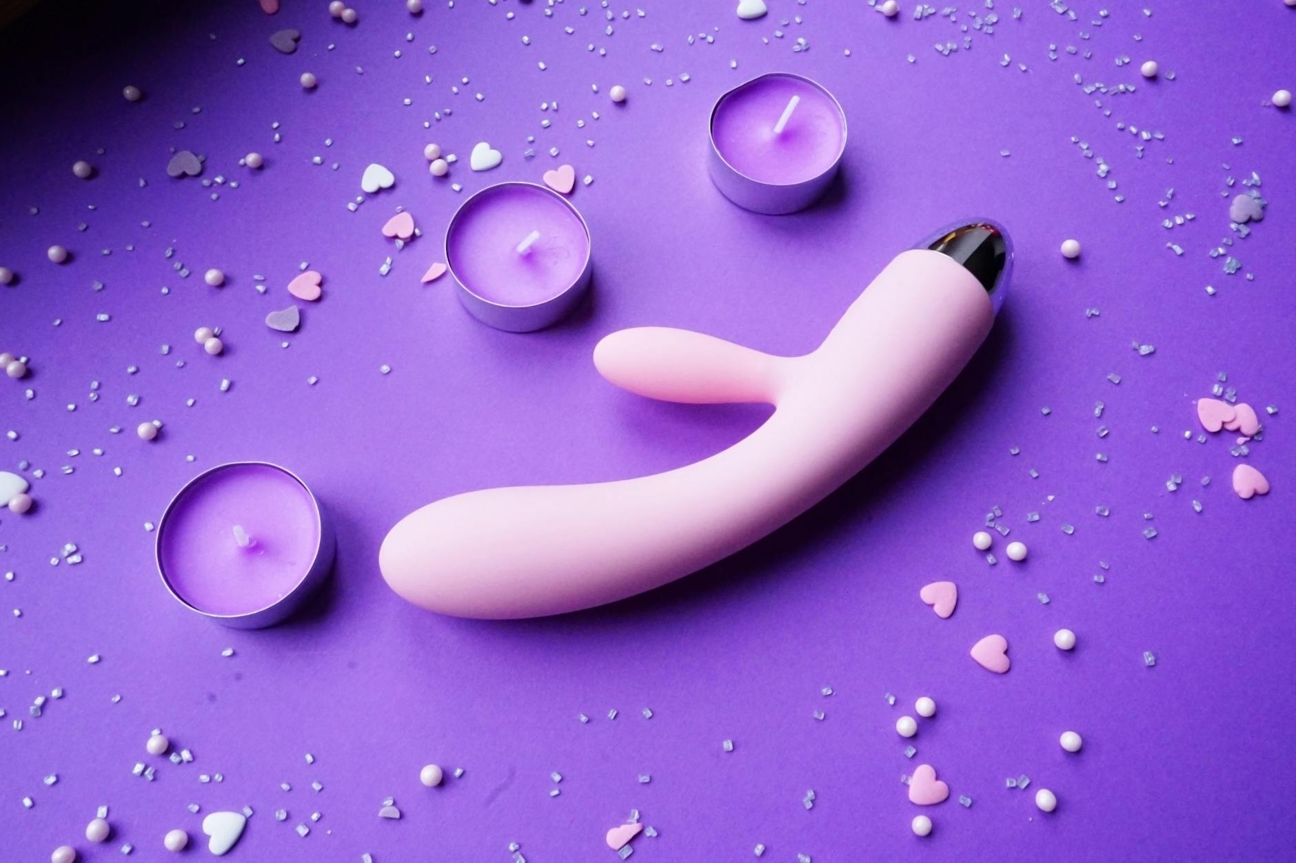 Vibrator with candles and confetti on purple background, romantic mood lighting
